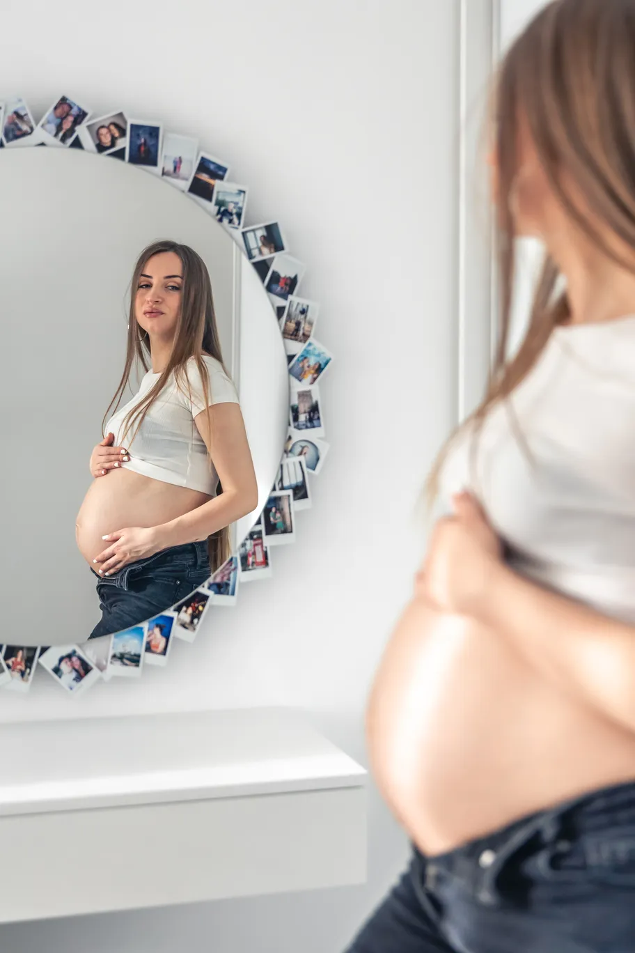 Imagen de una mujer en estado de embarazo mirando su figura en el espejo, considerando los cambios físicos que podrían tratarse con un procedimiento mommy makeover