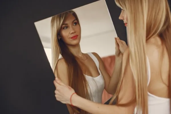 Mujer sosteniendo un espejo frente a ella observando el impacto de una cirugía plástica en su rostro.Mujer sosteniendo un espejo frente a ella observando el impacto de una cirugía plástica en su rostro.