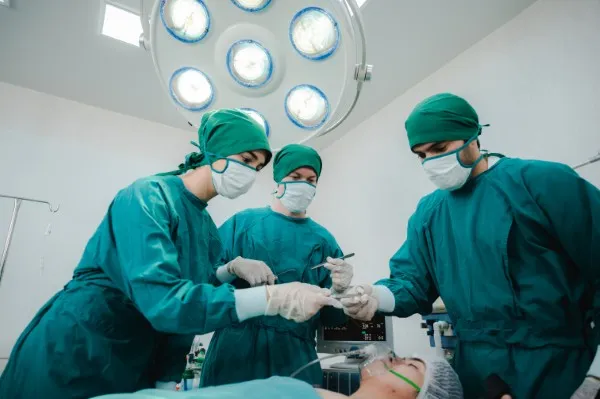 Un equipo de cirujanos profesionales realiza una operación bajo las luces del quirófano. La pregunta de a qué edad se puede hacer cirugía plástica es crucial en su práctica