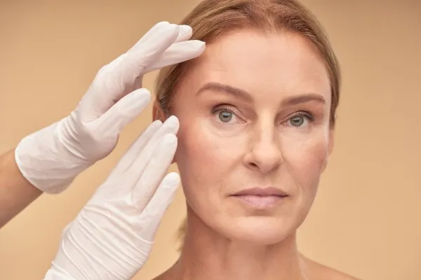 Especialista evalúa el rostro de su paciente para definir el lifting facial precio total y las necesidades de la paciente Lifting facial precio: factores que influyen en el tratamiento de una mujer mayor frente a especialista