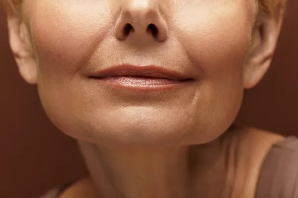 Imagen de la parte inferior del rostro de una mujer de edad avanzada que muestra arrugas y líneas de expresión antes de su mini lifting facial precio Zona donde se realiza el mini lifting facial en el rostro de una mujer con arrugas visibles