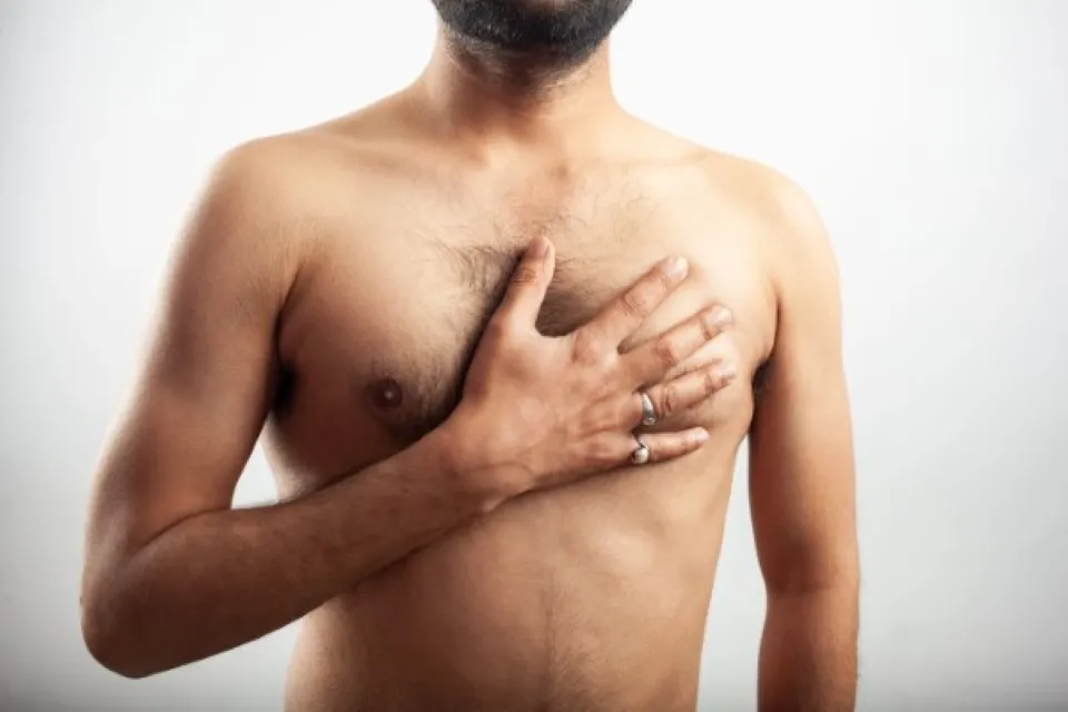 Primer plano de un hombre con dolor en el pecho, sosteniendo la mano sobre su seno, indicativo de sensibilidad por ginecomastia.