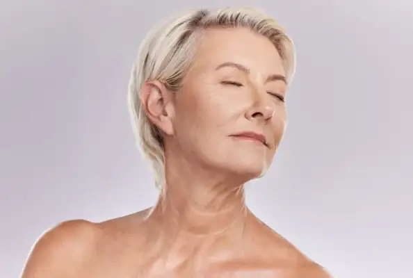 Una mujer mayor con cabello rubio corto y piel tersa aparece de perfil con los ojos cerrados, mostrando su tratamiento de rejuvenecimiento facial.